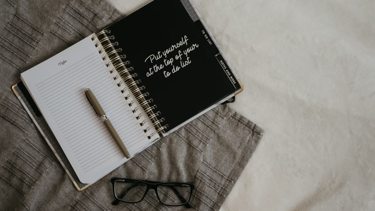 Stylish flatlay featuring a planner with quote, pen, and eyeglasses on a neutral background.